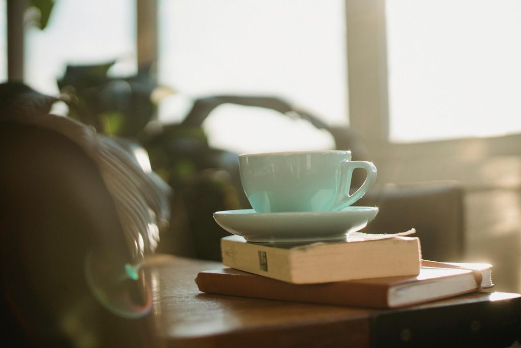 White ceramic cup of tea with plate and worn book with notebook placed on table Image