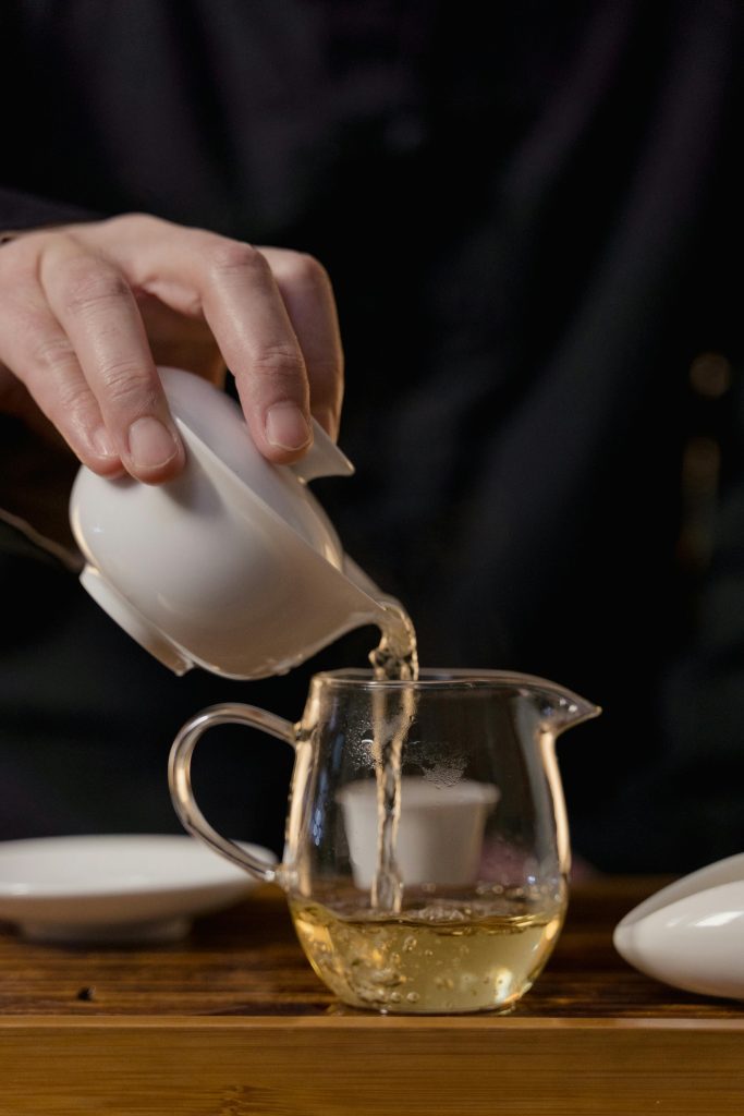 Pouring tea from a glass teapot with a ceramic covered bowl in hand Images